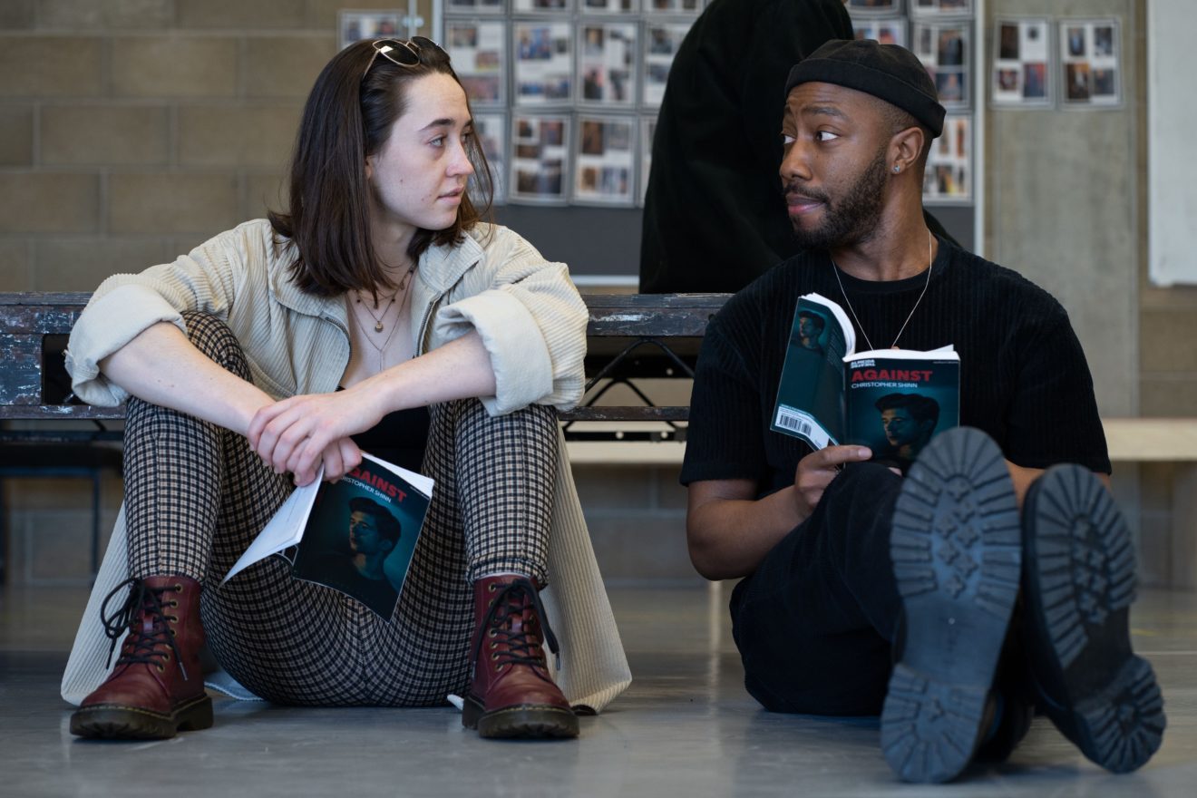 Two students are sitting on the floor with books, whilst looking at each other